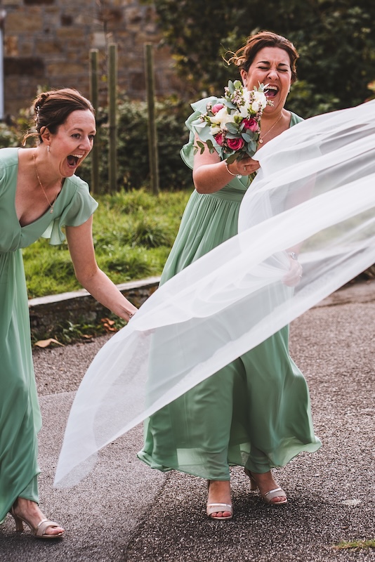 Candid photography of bridesmaids catching the wedding veil in the wind